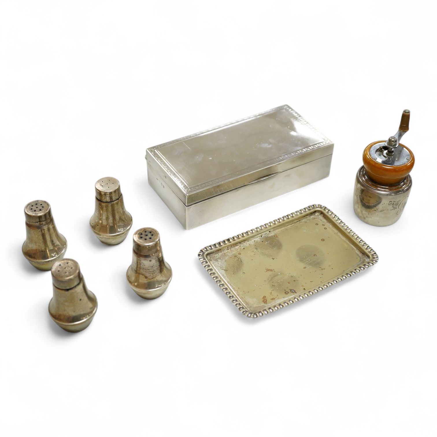 A George V engine turned silver mounted rectangular cigarette box, Birmingham, 1923, 17.7cm, a sterling mounted pepper grinder, four weighted sterling condiments and a small plated tray.